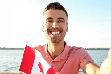 Tableaux ronds sur aluminium brossé Canada Young man with flag of Canada taking selfie near river