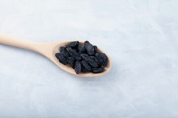 Sweet black raisins in wooden spoon on gray textured background. Dried grapes fruit. Selective focus, copy space