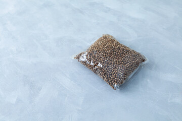 Dried coriander seeds in transparent plastic bag on grey background. Natural seasoning. Selective...