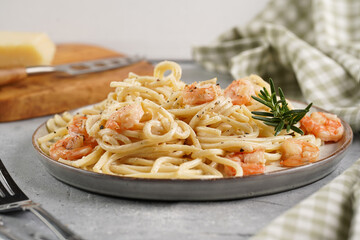 Deep grey japanese style bowl with pasta spaghetti with heavy cream and roasted shrimps with garlic sauce and parmesan cheese, black chopsticks on grey concrete surface