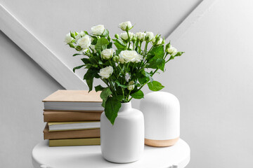 Vase with bouquet of beautiful roses, books and aroma diffuser on table near light wall