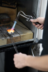 Cose-up of ceramic crucible with silver. Process of melting silver with gasoline burner. Male hands in frame. Jewelry Msterskaya. Inside oven hood. Blurred foreground.