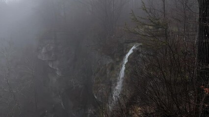 Waterfall over cliff into dense forest fog