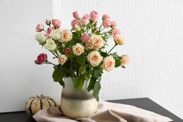 Vase with bouquet of beautiful roses and pumpkin on table