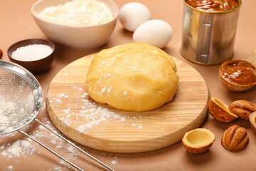 Wooden board of fresh dough for preparing walnut shaped cookies with boiled condensed milk and ingredients on brown background