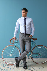 Handsome man in formal clothes with bicycle near color wall