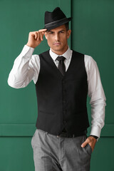 Gentleman in formal clothes wearing stylish hat on color background