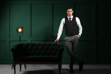 Fashionable gentleman standing near sofa in dark room