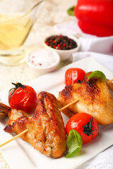 Plate with grilled chicken wings skewers and tomatoes on light background