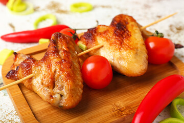 Wooden board with grilled chicken wings skewers with tomatoes on light background, closeup