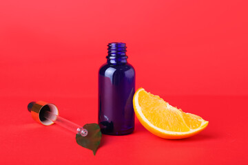 Bottle of essential oil and fresh cut orange on red background, closeup