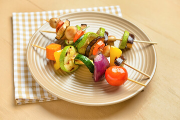 Plate with tasty vegetable skewers on wooden background, closeup