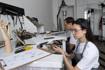 Young couple of craftsmen at their favorite work in their cozy workshop. They sit at workbench and...