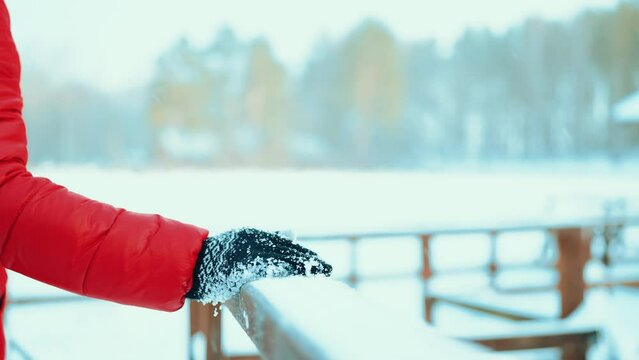 hand of a girl in a red jacket holds a snow-covered railing of the bridge on the background of a forest winter cold.