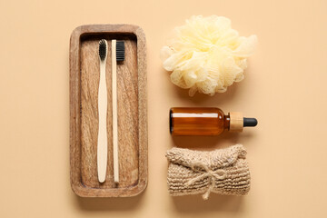 Wooden board with toothbrushes, bath sponges and bottle of essential oil on color background