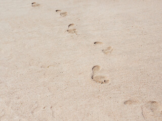 Male footprints on a sandy beach. A chain of bare footprints. Trail to follow. Outline of feet tracks.