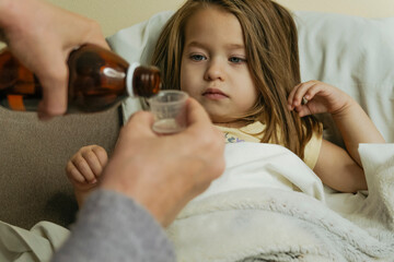 Obraz na płótnie Canvas Female hands pour medicine for sick little girl. 