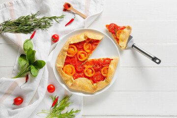 Plate with piece of tasty tomato galette on light wooden background