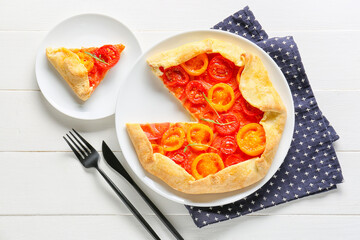 Plate with piece of tasty tomato galette on light wooden background