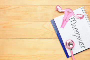 Notebook with word MENOPAUSE, paper uterus and stethoscope on light wooden background