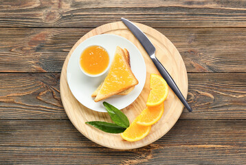 Board with tasty orange jam and bread on wooden background