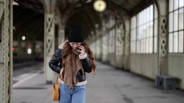 young woman is waiting train on station and calling by mobile phone, walking on platform