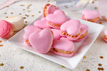 Plate with tasty heart-shaped macaroons on light background
