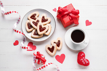 Plate with tasty cookies in heart shape, gift boxes and cup of coffee on light wooden background