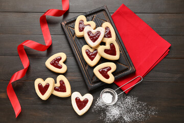 Board with tasty cookies and jam for Valentine's Day celebration on dark wooden background