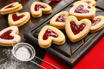 Board with tasty cookies and jam for Valentine's Day celebration on dark wooden background, closeup