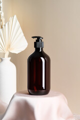 Dark amber glass dispenser cosmetic bottle design. Shampoo or shower gel container on podium with dried flowers on background.