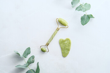 Face jade roller, gua sha, eucalyptus branches on stone surface. Flat lay, top view, overhead. © photoguns
