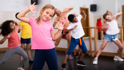 Portrait of little girl doing exercises during group class in dance center