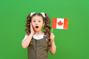 A surprised little girl has a Canadian flag on a green isolated background.