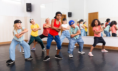 Obraz premium Multiethnic group of children in casual wear training hip hop movements in dance class with female coach..