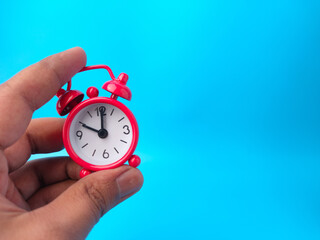 Hand holding red alarm clock on a blue background with copy space.