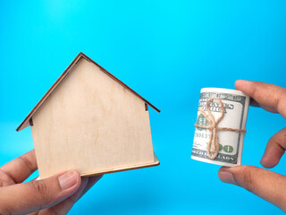 Hand holding wooden house and banknotes on blue background. Business concept.