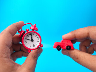 Hand holding clock and toys car on a blue background.