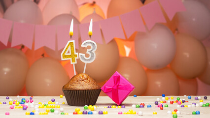 Decorations with balloons and a happy birthday candle with the number 43 for a woman. Happy birthday greetings in pink flowers for forty-three years old for an adult girl, copy space. Muffin 