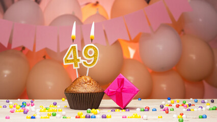 Decorations with balloons and a happy birthday candle with the number 49 for a woman. Happy birthday greetings in pink flowers for forty-nine years old for an adult girl, copy space. Muffin