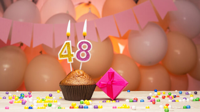 Decorations with balloons and a happy birthday candle with the number 48 for a woman. Happy birthday greetings in pink flowers for forty-eight years old for an adult girl, copy space. Muffin