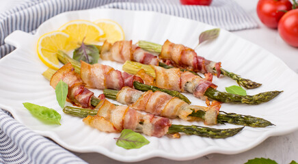 A dish of asparagus and bacon on a white plate. Baked green asparagus wrapped in bacon. Healthy food.