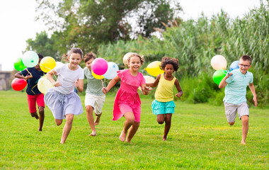 Group of happy kids running through grass with balloons in hands.