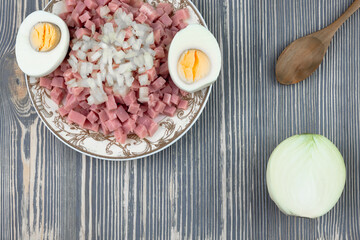 Sausage cut into small cubes and an egg in a plate. Peeled onion on the table. We make a salad.