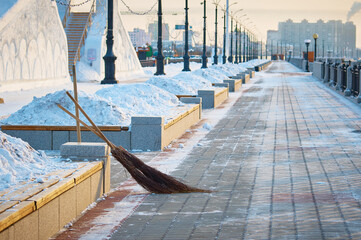 Two brooms. City embankment on a winter morning after snow removal. Flower beds with snowdrifts. Promenade fencing with lanterns and benches. Selective focus. Blagoveshchensk, Russia.