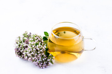 Herbal tea in a glass cup, fresh oregano flowers on a light background. Medicinal plants. The drink...