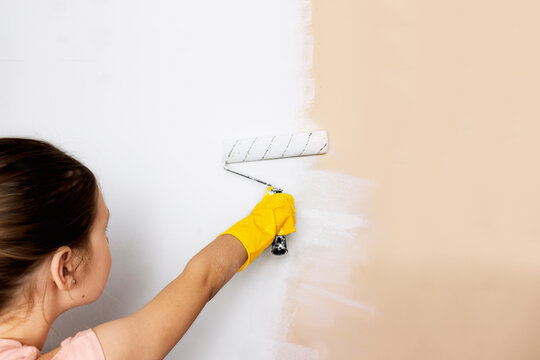 home repairs. painting walls with paint. renovation.
girl child in yellow gloves paints a wall with a roller with white paint.
