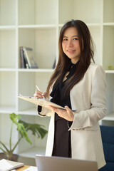 Female boss standing and holding a business clipboard in office.