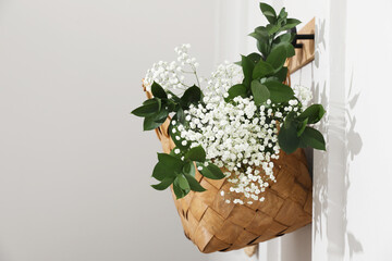 Stylish wicker basket with bouquet of flowers hanging on wooden rack indoors, space for text