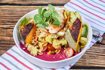 A serving of grilled chicken salad with vegetables in a round white bowl